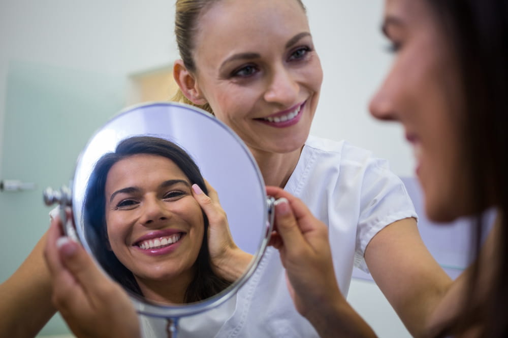 Mulher jovem analisando o rosto no espelho em clínica estética