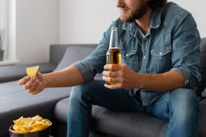 homem bebendo cerveja e comendo salgadinhos