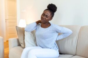 Mulher adulta sentada no sofá, demonstrando desconforto físico.